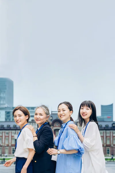 four business women lined up with smiles outdoors