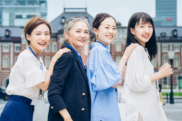 four business women lined up with smiles outdoors