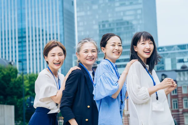 four business women lined up with smiles outdoors