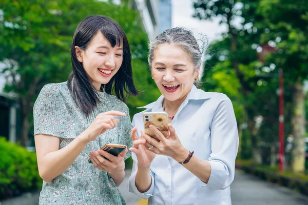 mother and daughter using smartphones outdoors