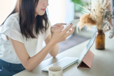 A woman operating a smartphone in front of a PC screen