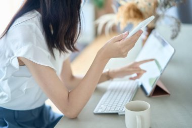 A woman operating a smartphone in front of a PC screen