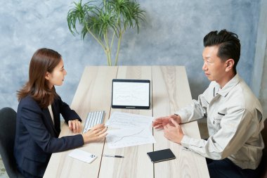 A woman in a suit meeting with a man in work clothes at office