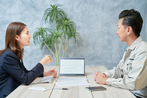 A woman in a suit meeting with a man in work clothes at office