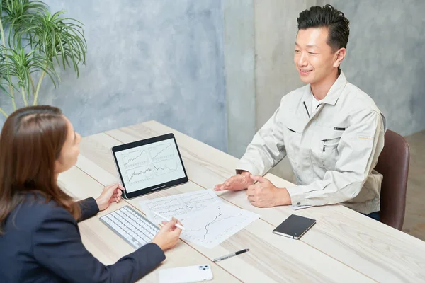A woman in a suit meeting with a man in work clothes at office