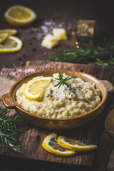 Lemon rice risotto with rosemary on dark wooden background, vertical