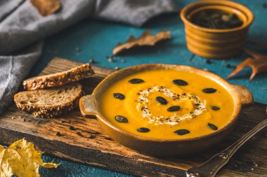 Kremalı balkabağı çorbası ve tohumlar mavi arka planda, ahşap bir tahta üzerinde