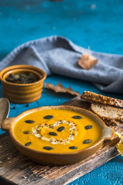 Kremalı balkabağı çorbası ve tohumlar mavi zemin üzerinde ahşap bir tahta üzerinde, kopyalama alanı ile dikey