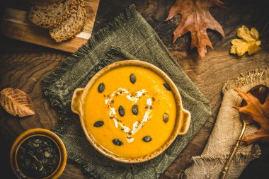 Kremalı balkabağı çorbası ve kırsal metalde tohumlar ve sonbahar yapraklı ahşap arka plan, üst manzara.