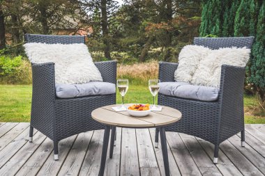 Yastıklı iki rattan sandalye ve ahşap terasta şarap kadehli küçük bir masa.
