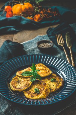 Kırsal ahşap arka planda mavi bir tabakta otlu küçük balkabağı krepleri, dikey 
