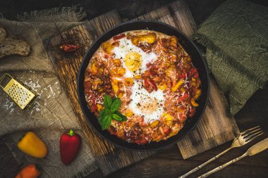 Shakshuka tahta arka planda demir bir tavada. Geleneksel Orta Doğu yemeği. Domatesli sahanda yumurta, dolma biber, sebze ve otlar. Üst görünüm.