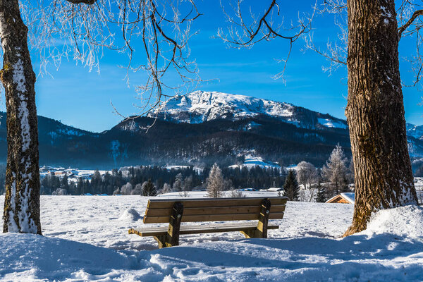 Скамейка в снежном ландшафте солнечным зимним утром