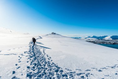 Turistler, güneşli bir kış gününde Norveç 'in Troms kentindeki Storsteinen Dağı' nın zirvesinde yürüyüş parkurunda yürüyorlar.