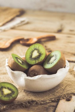 Kırsal ahşap bir masada, beyaz bir kasede yarım kivi.