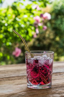 Lezzetli kırmızı meyve suyu ya da ahşap bir bahçe masasında altın metal kamışlı kokteyl içeren güzel süs bardağı.