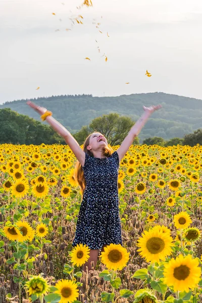 Teenage girl in sunflower field throwing petals in the air. Arms in motion, focus on the face. Vertical.