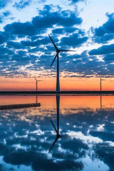 Wind turbines in the light of the sunset with a beautiful reflection in the water, vertical.
