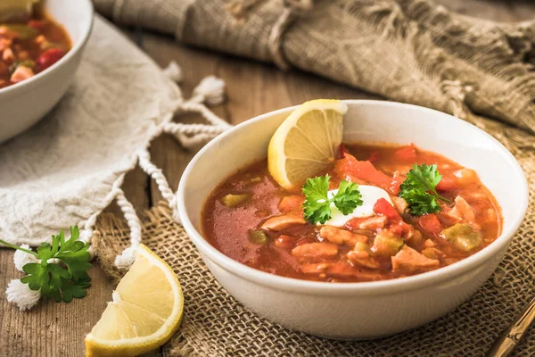 Bowl with Solyanka, a spicy and sour soup of Russian origin, on wooden background. Soljanka is well known in East European countries and East Germany