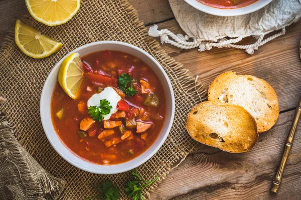 Bowl with Solyanka, a spicy and sour soup of Russian origin, on wooden background. Soljanka is well known in East European countries and East Germany. Top view.