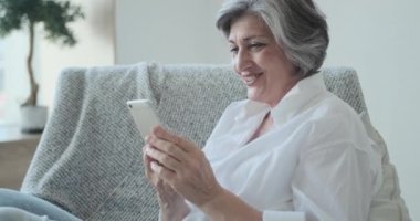 Gülümseyen 60 'lı yaşlarda orta yaşlı bir bayan video konferansı için cep telefonundan zevk alıyor.