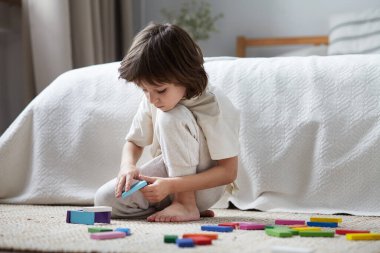 Hevesli anaokulu öğrencisi yatak odasında kendinden emin bir şekilde renkli tahta bloklar inşa ediyor.