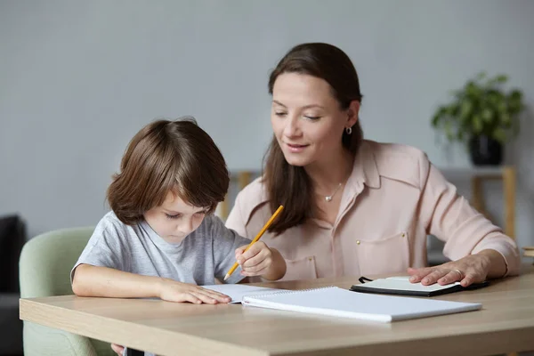 Domácí výuka malého krásného chlapce, který se učí psát a malovat. Mladá krásná matka instruktor — Stock fotografie