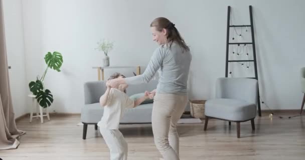 Zabawny przedszkolak bawi się z matką trzymając się za ręce tańcząc i skacząc razem — Wideo stockowe