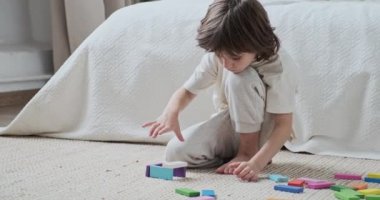 Zeki erkek çocuk, çok renkli ahşap tuğla bloklar inşa ederek eğlence etkinliği geliştiriyor.