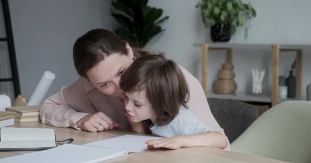 Привлекательная молодая мать учится дома со своим ребенком-учеником и учит его считать и писать. — стоковое видео