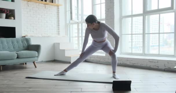 Atletisk ung kvinna sträcker ben och armar hemma med stora fönster på morgonen. — Stockvideo