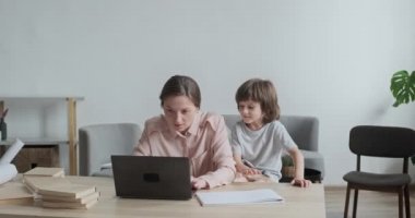 Serbest çalışan anne bilgisayarda daktilo ve uzaktan çalışmaya odaklanmış durumda. Huzursuz çocuk masaya çıkıyor.