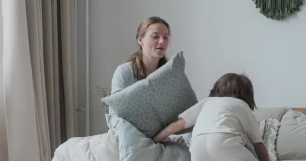 행복 한 소년 이 베개를 가지고 놀고 있는 모습 과 집에서 침대에서 뛰는 미소짓는 베이비 시터가 싸우는 모습 — 비디오