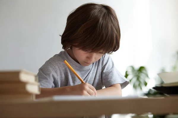 Niño de 6 años reflexivo y considerado, atento y trabajador que aprende a escribir y dibujar en casa. — Foto de Stock