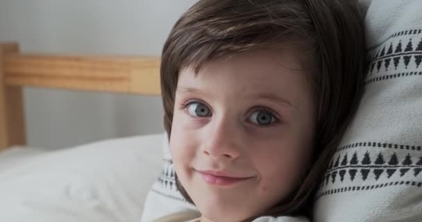 Retrato bonito menino com olhos azuis morena cabelo deitado em travesseiro confortável relaxante em casa — Vídeo de Stock