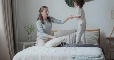 Gülen anne, oynaşan sevimli çocukla oynuyor. Yatak odasında rahat bir yatakta zıplıyor.