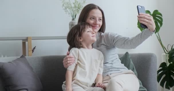 微笑的母亲和小儿子摆出一副自拍的样子，用智能手机放松地享受家庭周末 — 图库视频影像