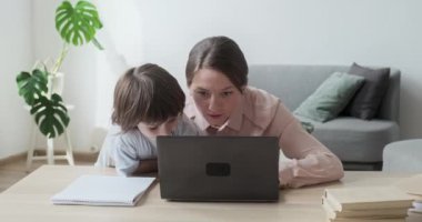 Anne ve oğlu birlikte dizüstü bilgisayar kullanıyor, internette geziniyor, alışveriş yapıyor ve oyunlar oynuyorlar..