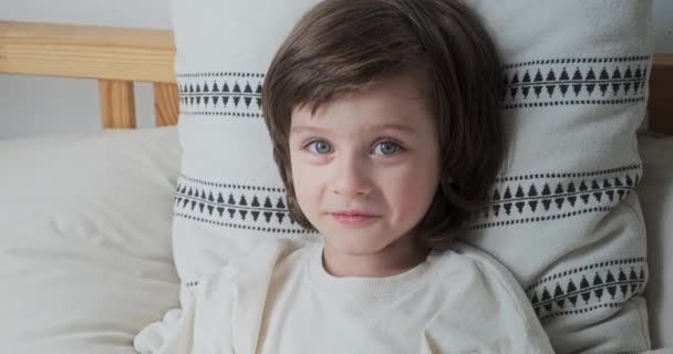Πορτρέτο χαμογελαστό χαριτωμένο αρσενικό παιδί χαλαρώνοντας σε άνετο μαξιλάρι έχοντας θετικό συναίσθημα — Αρχείο Βίντεο