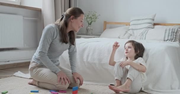 Счастливая мать и маленький сын разговаривают друг с другом, играя деревянные кубики кирпича наслаждаясь дружбой — стоковое видео