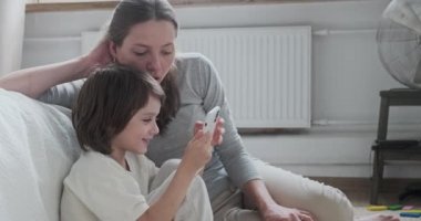 Şok olmuş kadın bebek bakıcısı ve gülümseyen çocuk online video oyunları oynarken akıllı telefon kullanıyor.