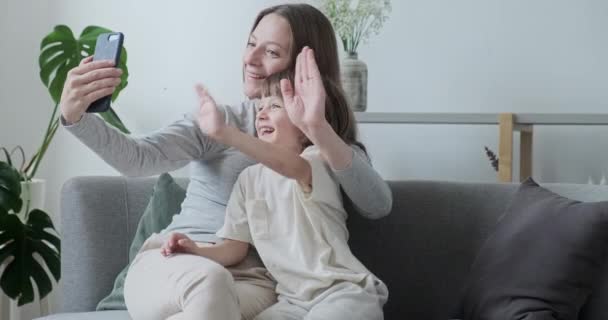 Mosolygós bébiszitter és kisfiú beszél online video hívás üdvözlő integető kéz használata okostelefon — Stock videók