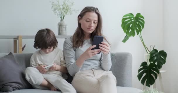 Focalisé moderne mère et fils enfant bavarder surf utilisation d'Internet smartphone assis sur le canapé ensemble — Video