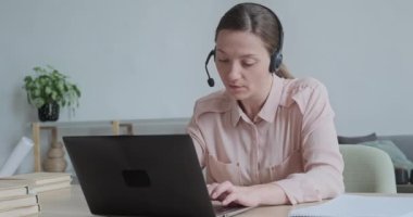 Ciddi bir beyaz kadın video ile konuşuyor ve dizüstü bilgisayara bakıyor ve daktilo yazıyor..
