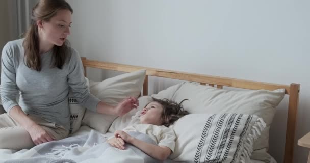 Мать беспокоилась о здоровье сына проверить горячий лоб лежа на подушке кровати. Дошкольник чувствует головную боль — стоковое видео