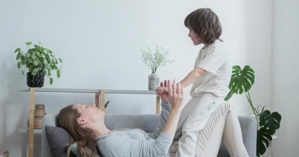 Schöne junge fröhliche Mutter spielt aktiv mit ihrem niedlichen kleinen Sohn, kuschelt sich in die Luft — Stockvideo