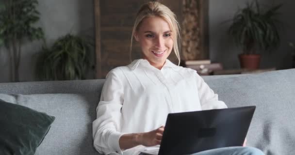 Ευτυχισμένο χαριτωμένο ξανθιά γυναίκα κουβέντα surfing internet χρήση φορητού υπολογιστή κάθεται στον καναπέ στο γραφείο στο σπίτι — Αρχείο Βίντεο