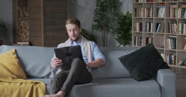 Nachdenklicher Jungunternehmer tippt auf Laptop sitzend Sofa bei hom — Stockvideo