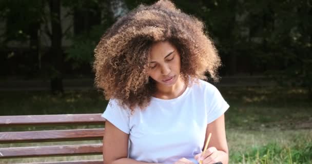 Pensive gemengde ras vrouwelijke handschrift papier notities in notitieblok pagina gebruik potlood — Stockvideo