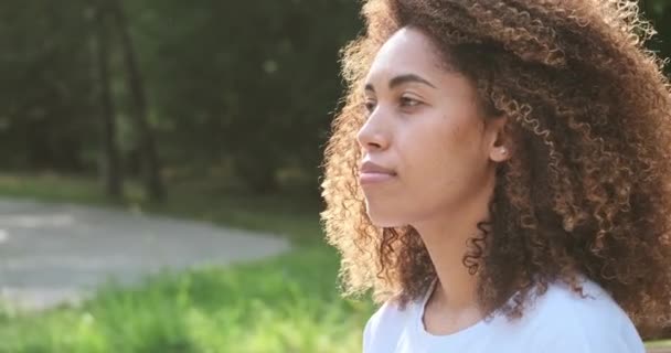 Junge schwarze Frau setzt sich draußen im Park eine medizinische Maske auf und sitzt auf einer Bank. — Stockvideo